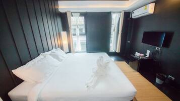 A hotel room with a neatly made bed, a flat-screen TV mounted on the wall, and a window with curtains.