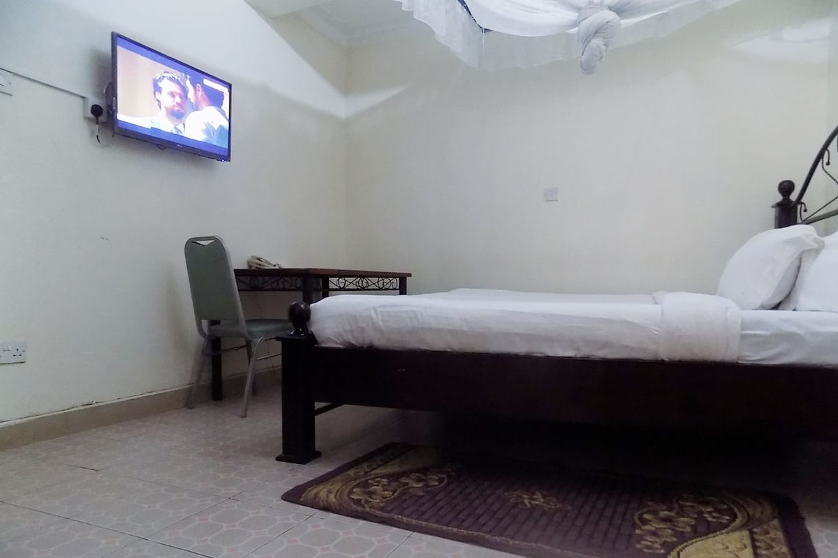 A bedroom with a bed, a desk, a chair, and a television on the wall.