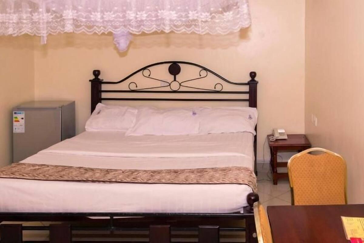 A single bed with a headboard, a bedside table, a chair, and a small desk with a telephone.