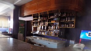 Una zona de bar con encimera de mármol, estantes llenos de botellas de licor y un monitor de ordenador.