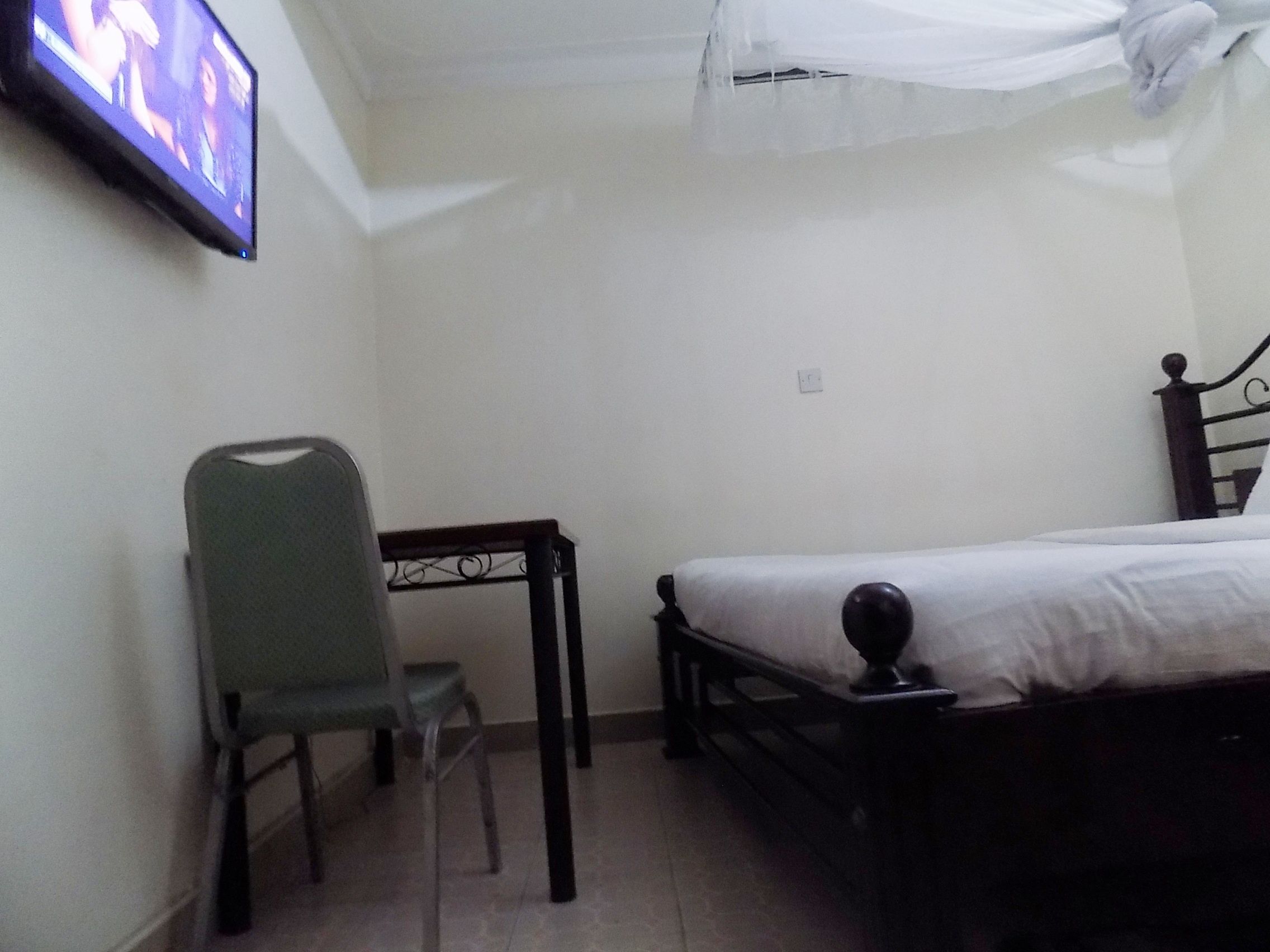 A bedroom with a bed, a chair, a small table, and a TV mounted on the wall.