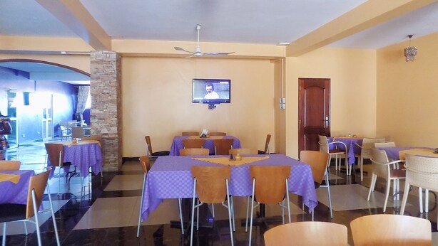 Un comedor con varias mesas y sillas, un televisor en la pared y un ventilador de techo.