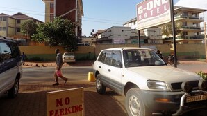 Un edificio con un letrero que indica G-One Hotel, una señal de prohibido estacionar y un automóvil estacionado.