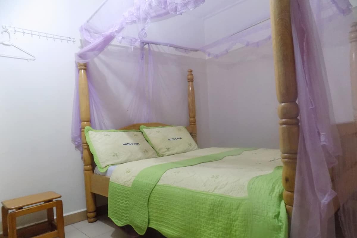 A four-poster bed with a green bedspread and two pillows labeled "HOTEL PLUS".