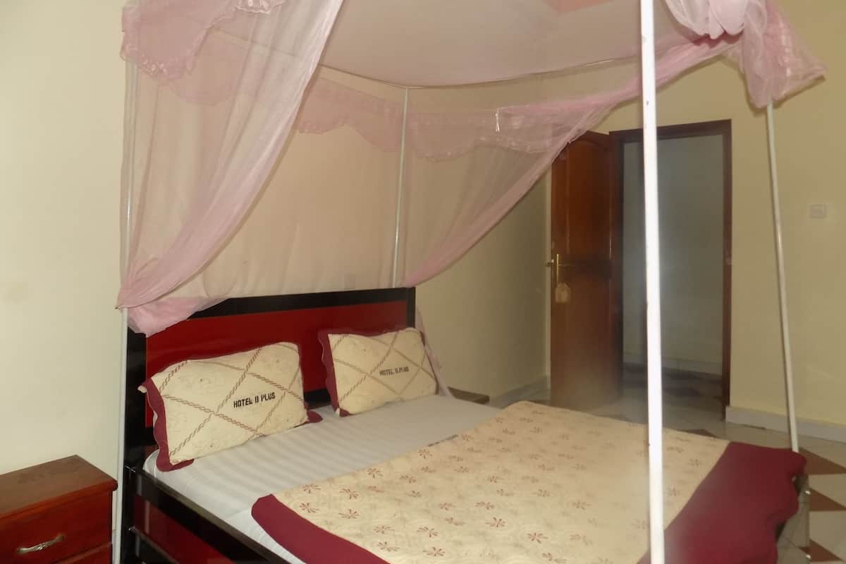 A single bed with a canopy, two pillows with 'HOTEL D PLUS' branding, a red headboard, and a wooden nightstand.