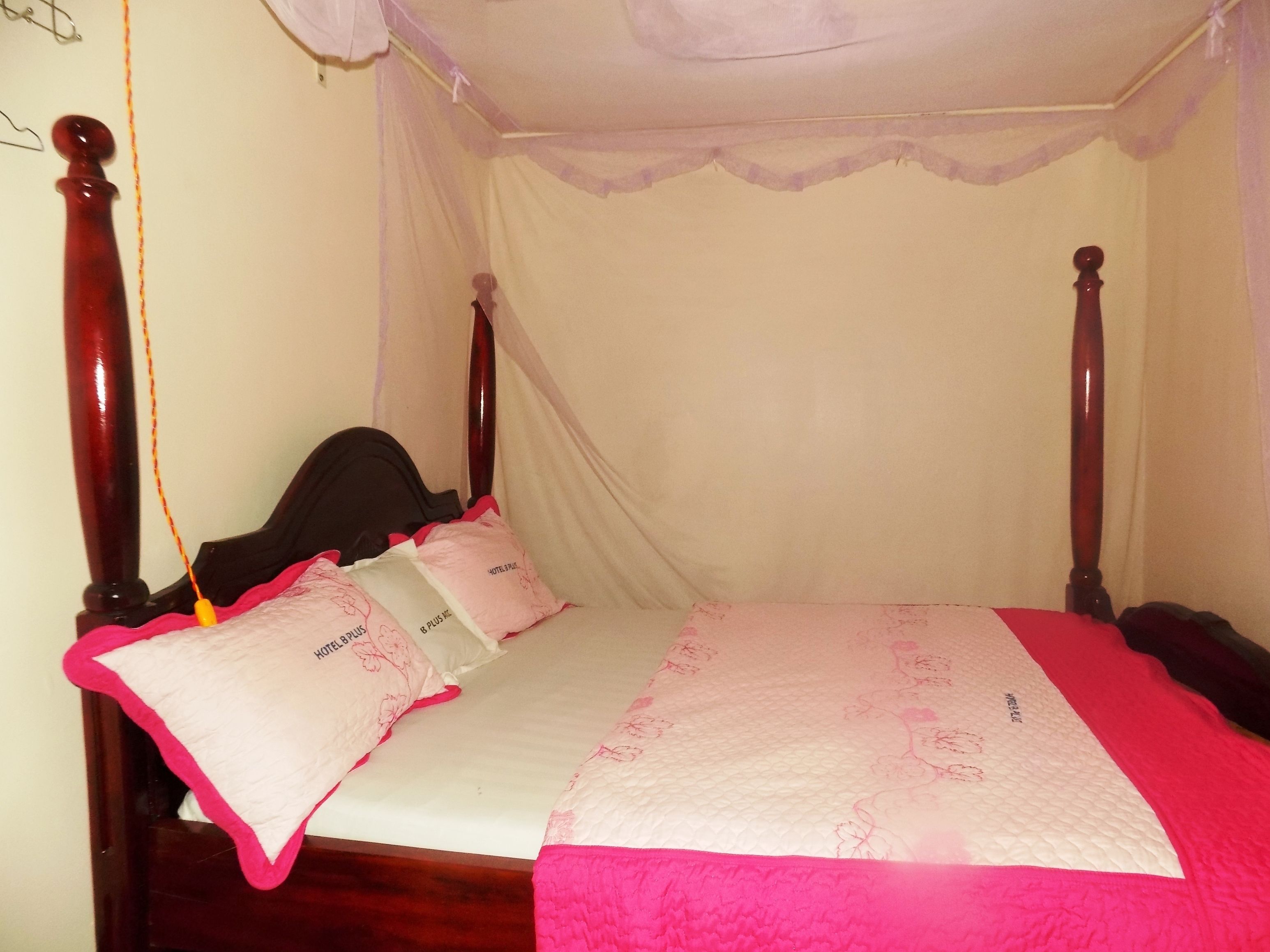 A four-poster bed with a canopy, a bedspread, and pillows with a hotel logo.