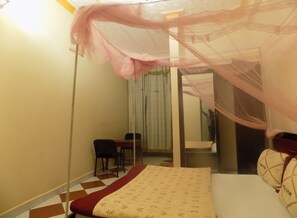 A bedroom with a bed, a chair, a table, and a mirror. - Hotel B Plus (Mbarara)