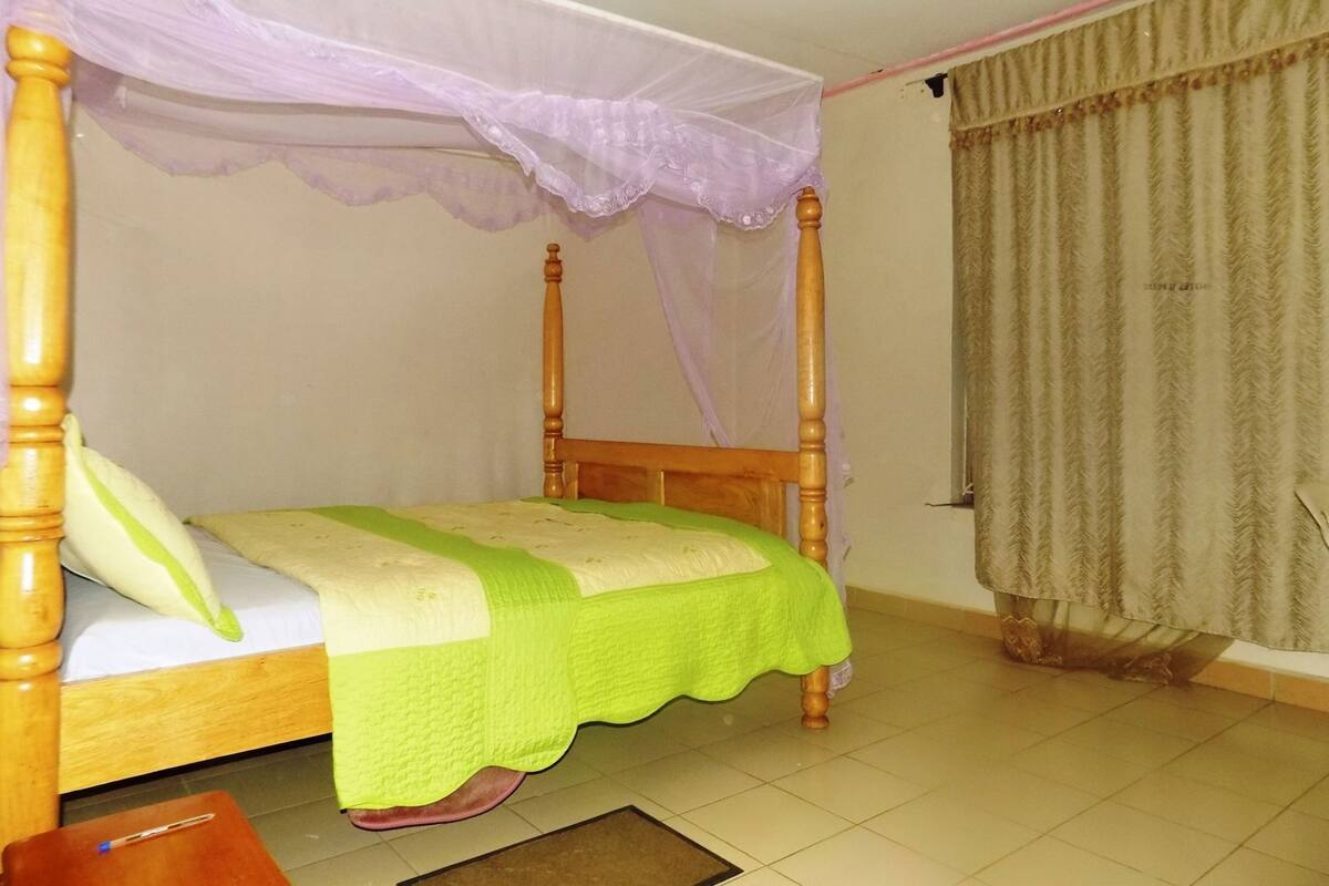 A four-poster bed with a green bedspread, a wooden headboard, and a canopy.
