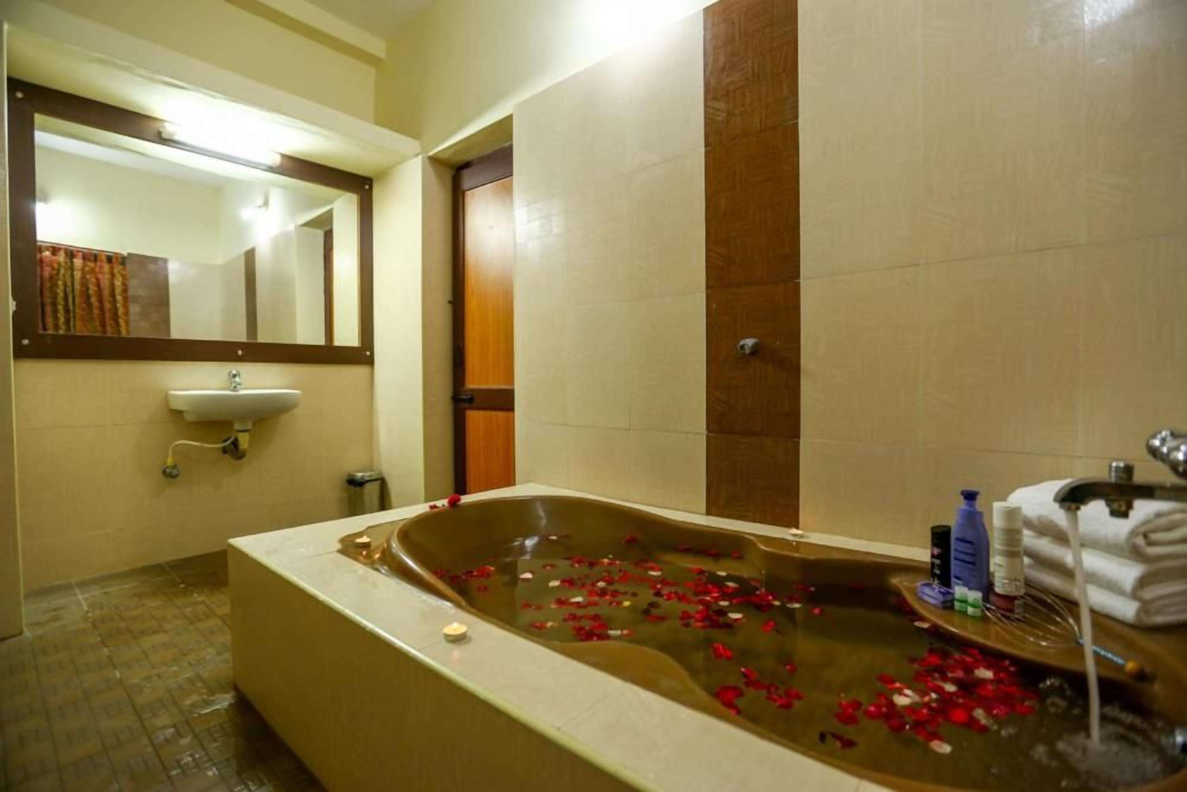 A bathroom with a bathtub filled with water and rose petals, a sink, and a mirror.