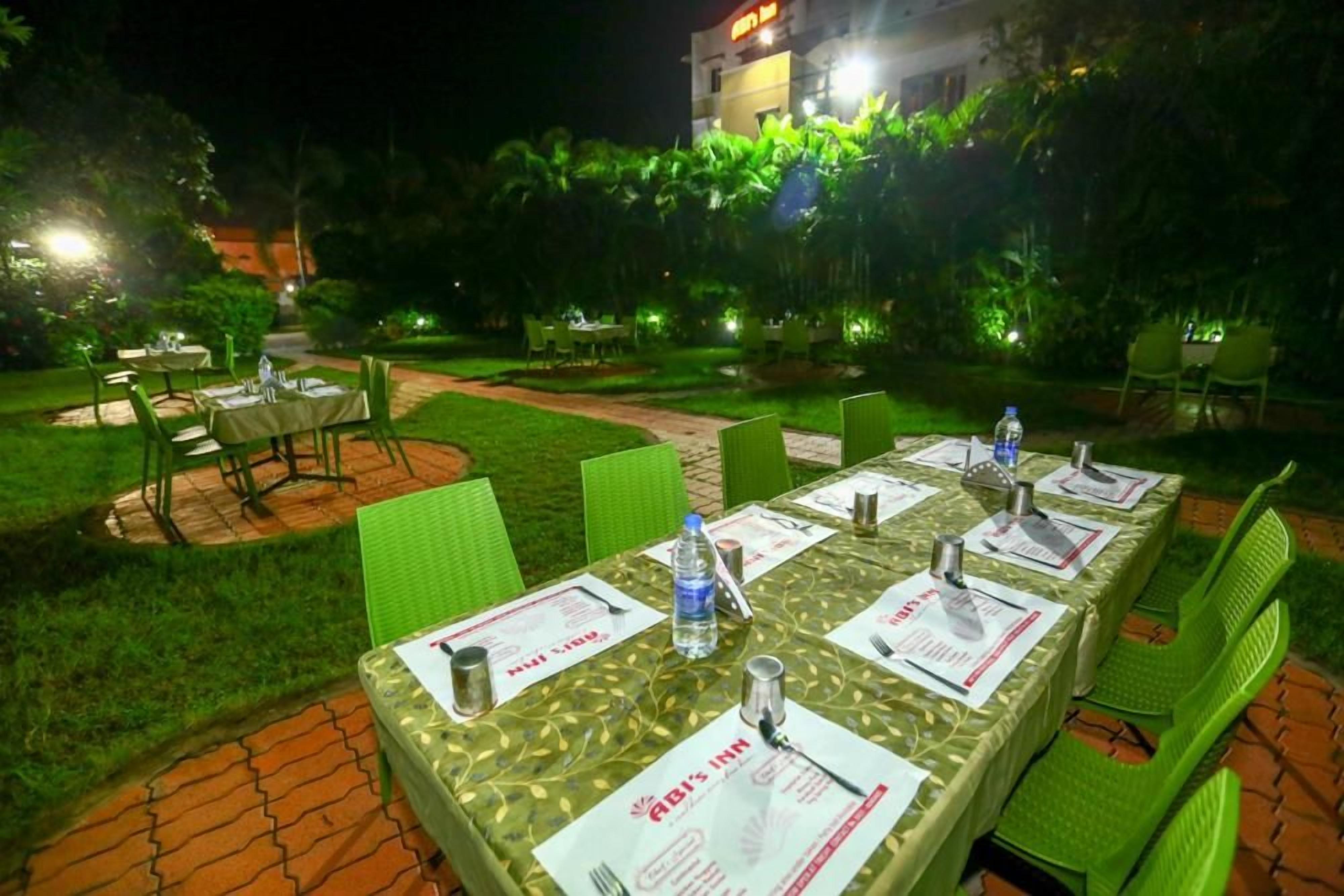 Un área de comedor al aire libre con mesas dispuestas para dos, sillas verdes y un sendero de jardín bien iluminado.