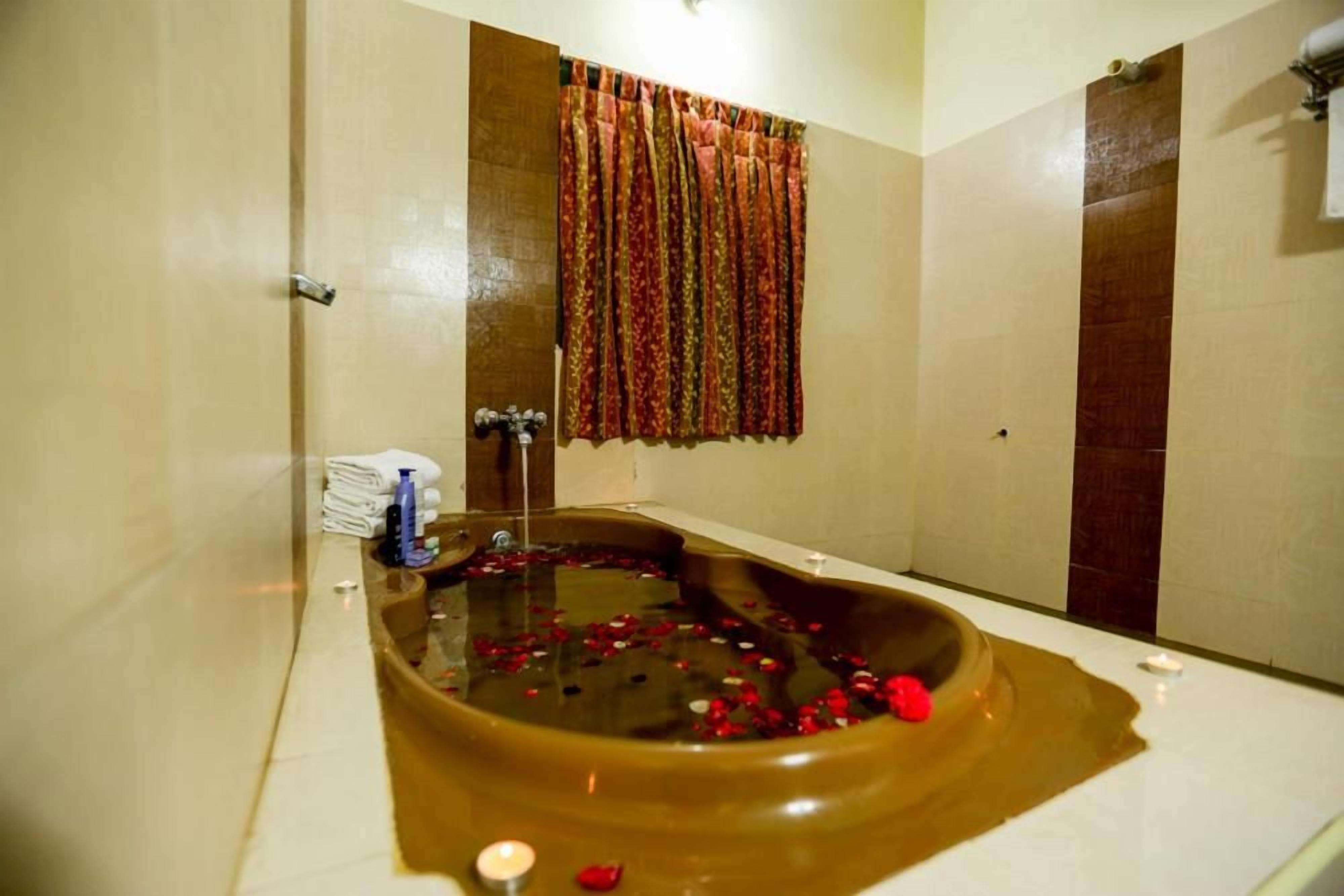 Ein Badezimmer mit einer großen Wanne, gefüllt mit Wasser und Rosenblüten, einem Handtuchhalter mit gefalteten Handtüchern und einer Duschkabine.