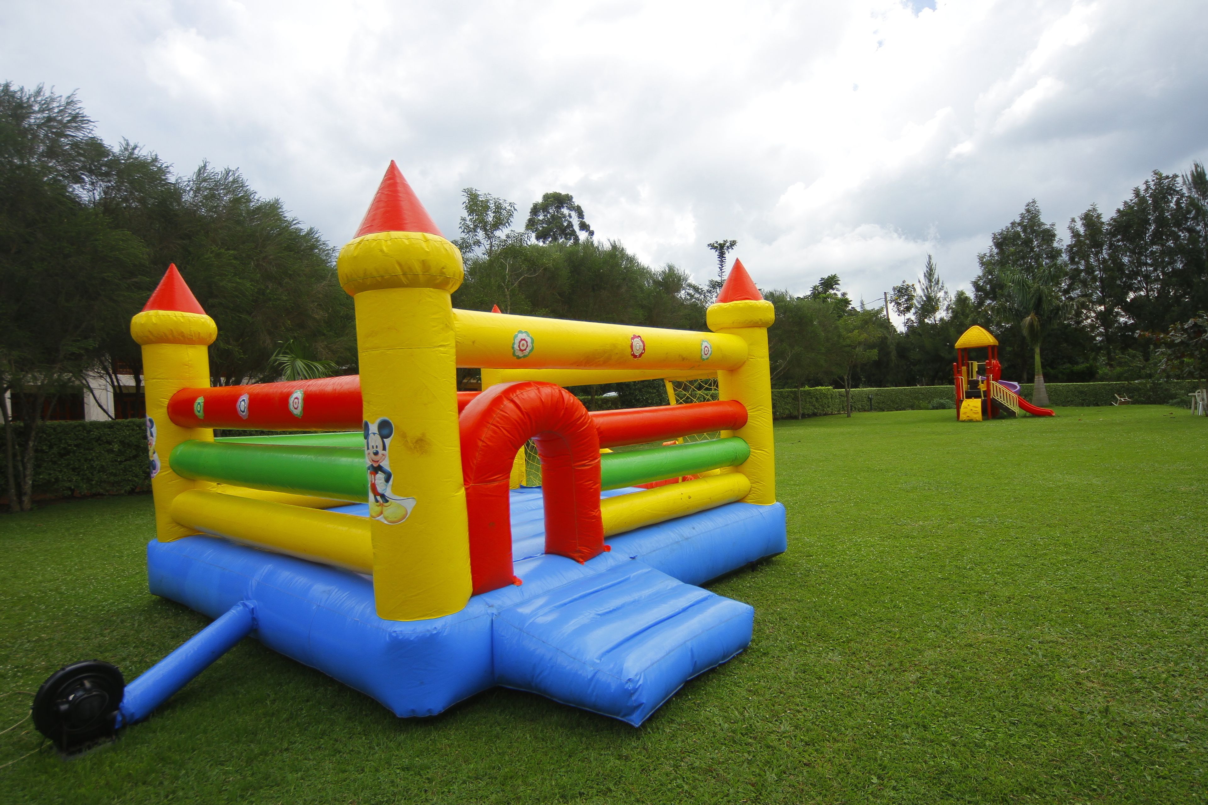 An inflatable bouncy castle with a slide and a small playhouse in a grassy area.
