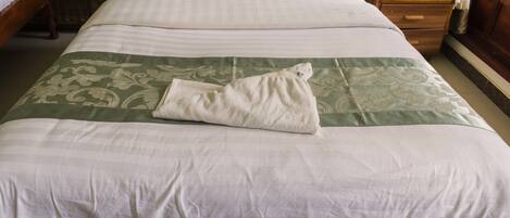 A neatly made bed with a green and white bedspread, a white pillow, and a folded towel on the bed.
