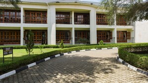 A multi-story building with a symmetrical facade, large windows, and a paved entrance area with a sign indicating an exit. - Kalya Courts Hotel (Fort Portal)