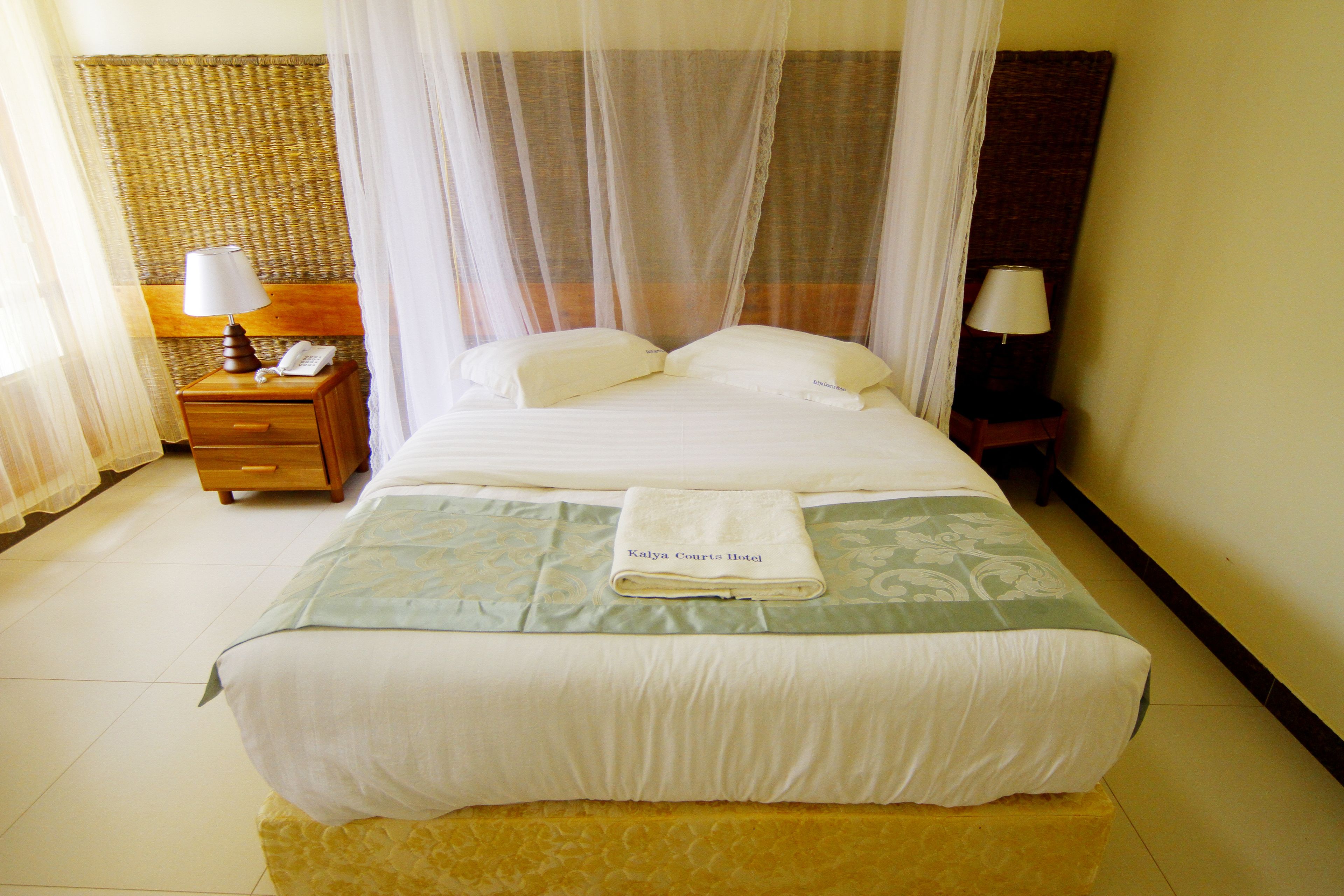 A neatly made bed with a folded towel, a bedside table with a lamp, and a nightstand with a telephone.