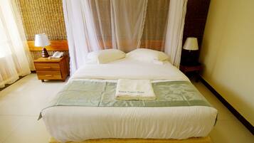 A neatly made bed with a folded towel, a bedside table with a lamp, and a nightstand with a telephone.