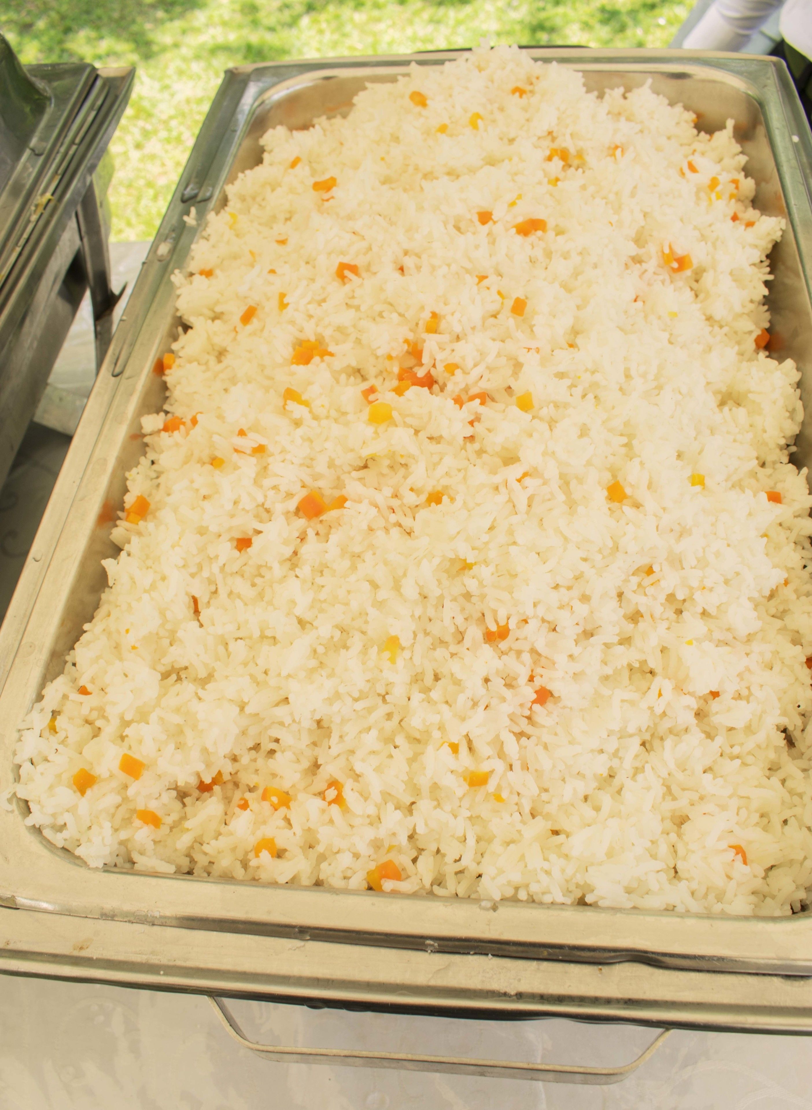 Ein Büfettisch mit einer großen Portion weißem Reis, vermischt mit orangefarbenen und gelben Stücken, wahrscheinlich Karotten und Erbsen.