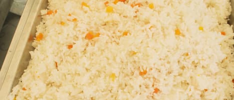Ein Büfettisch mit einer großen Portion weißem Reis, vermischt mit orangefarbenen und gelben Stücken, wahrscheinlich Karotten und Erbsen.