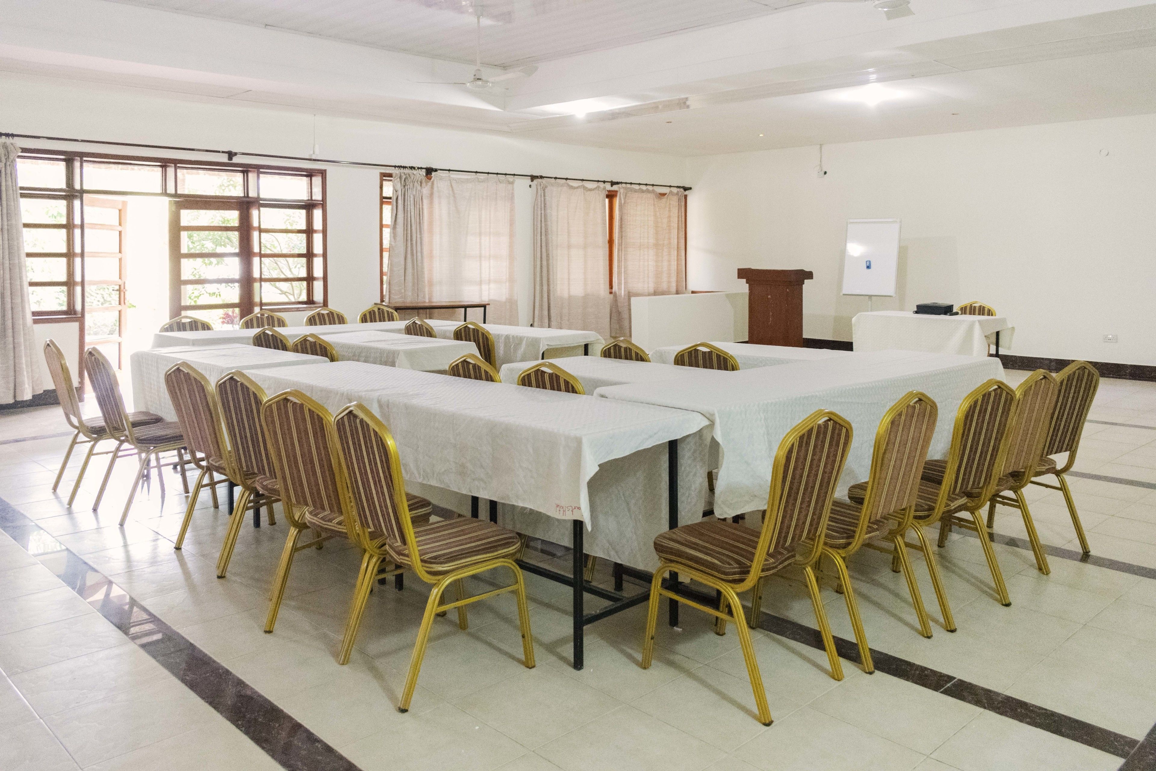 Un salón de conferencias con varias mesas y sillas, una pizarra y un atril.