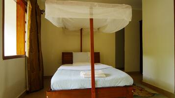 A single bed with a wooden frame and a canopy, a window with curtains, and a cartoon character rug on the floor.