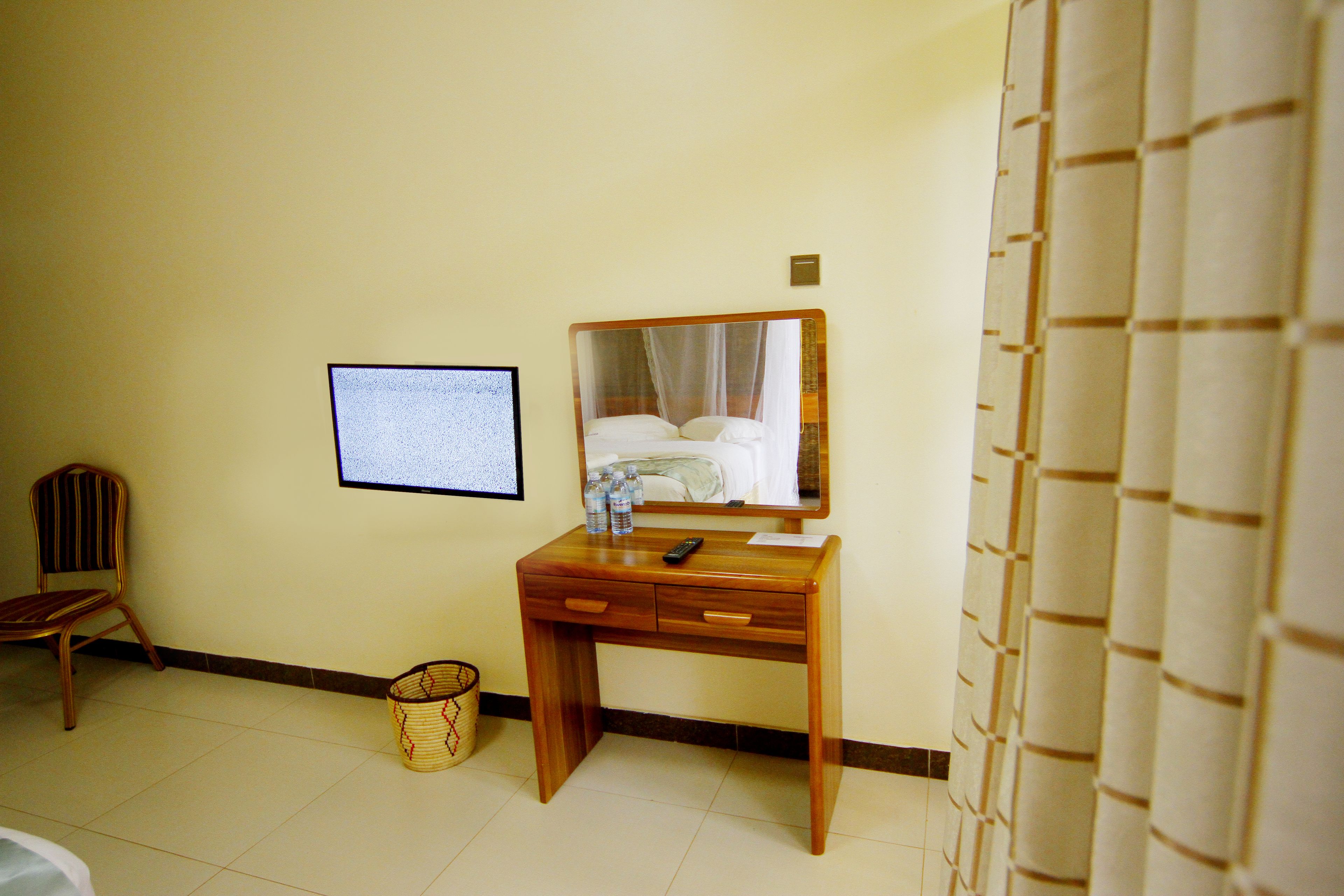 Een hotelkamer met een houten bureau, een stoel, een bed met hemel en een televisie, plus een gordijn.