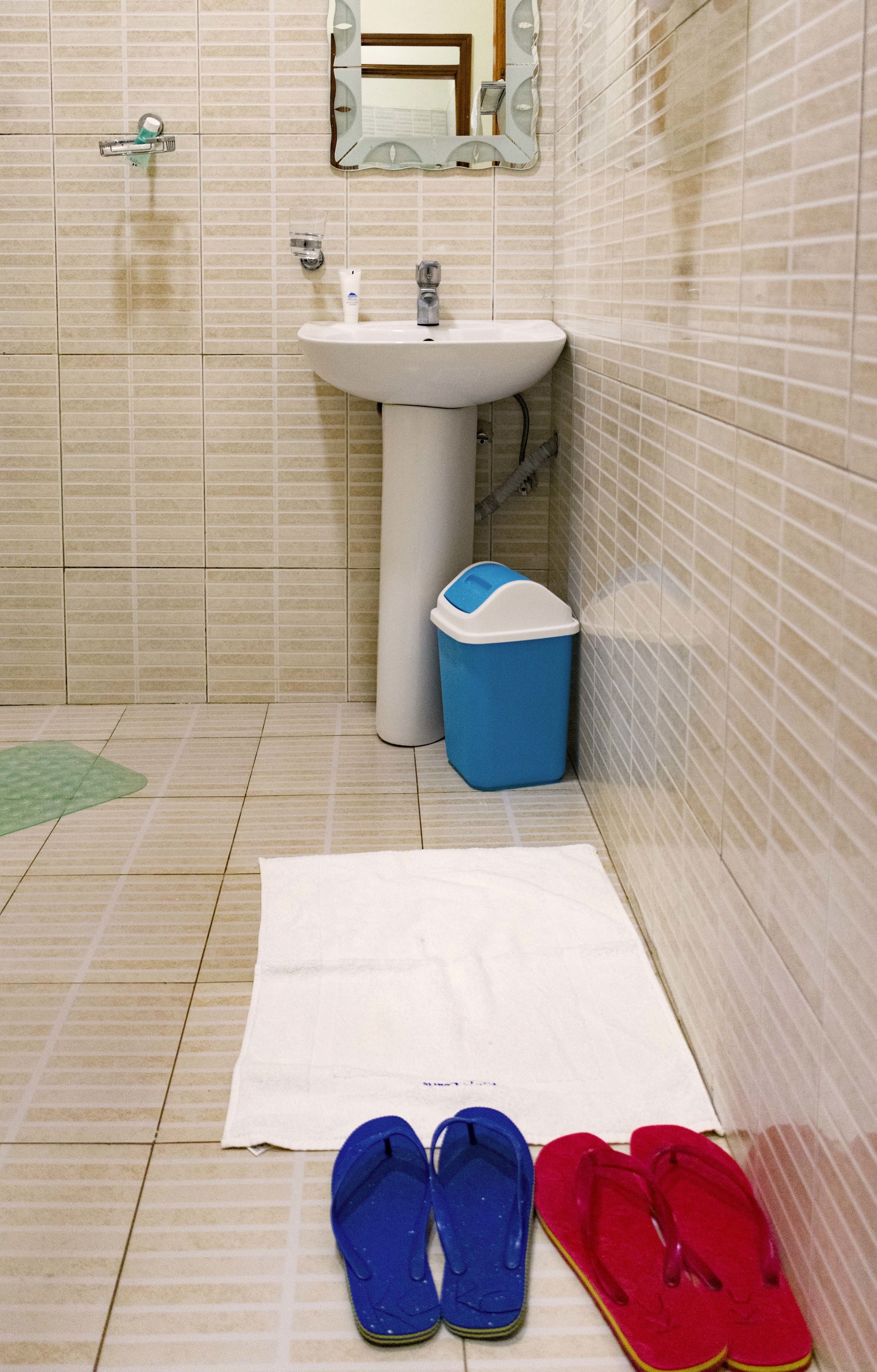 A bathroom with a sink, mirror, and a trash bin.