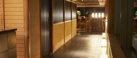 A corridor with wooden sliding doors, a tiled floor, and a seating area with tables and chairs.