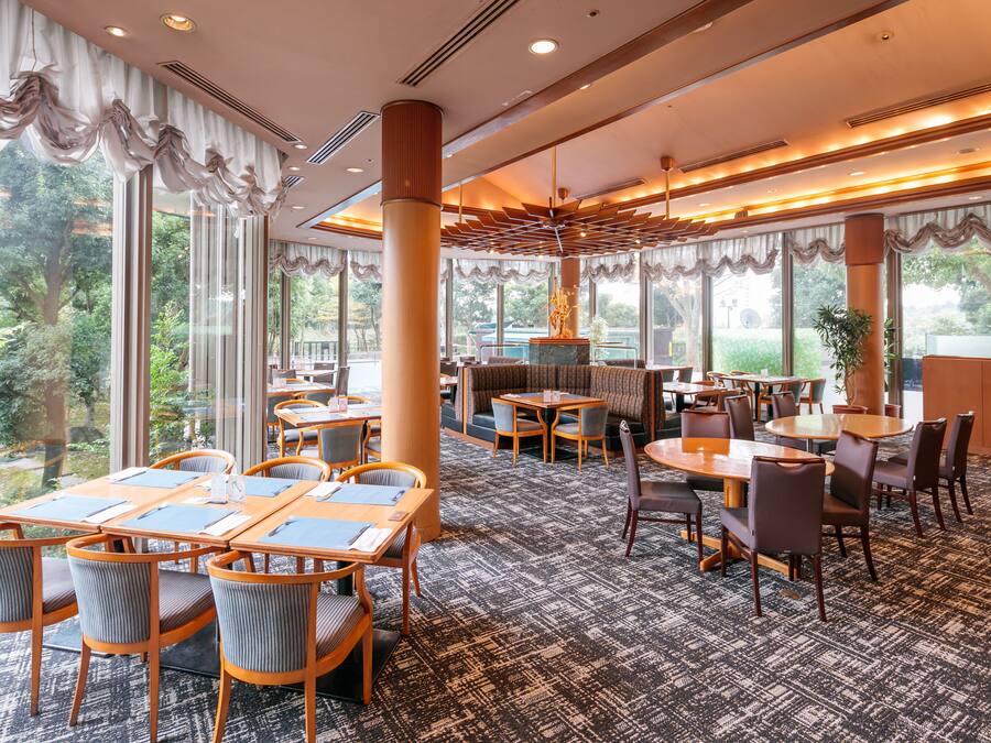 A spacious restaurant with high ceilings, large windows, and a variety of seating arrangements including booths and tables.