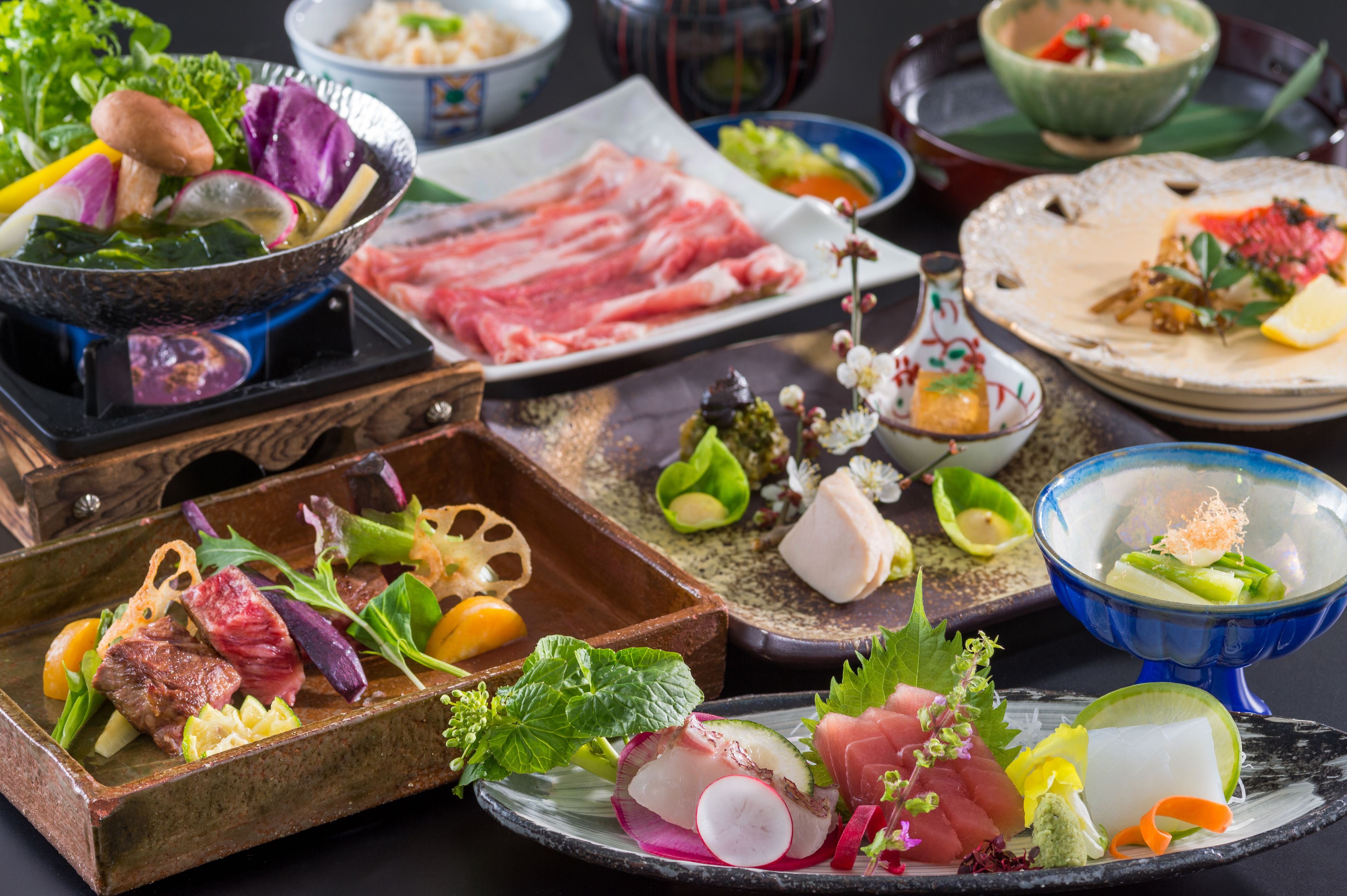 A variety of dishes including sashimi, vegetables, and meat, arranged on a table.
