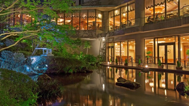 Un hôtel doté d’une cour paisible, agrémentée d’un bassin d’eau aux reflets changeants, d’une végétation luxuriante et d’un bâtiment de style traditionnel, orné de nombreux balcons et illuminé d’une lumière chaleureuse.