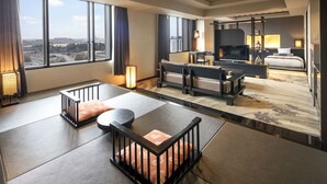 Une chambre d’hôtel moderne avec un sol recouvert de tatamis, un canapé, une télévision et un balcon offrant une vue sur la ville.