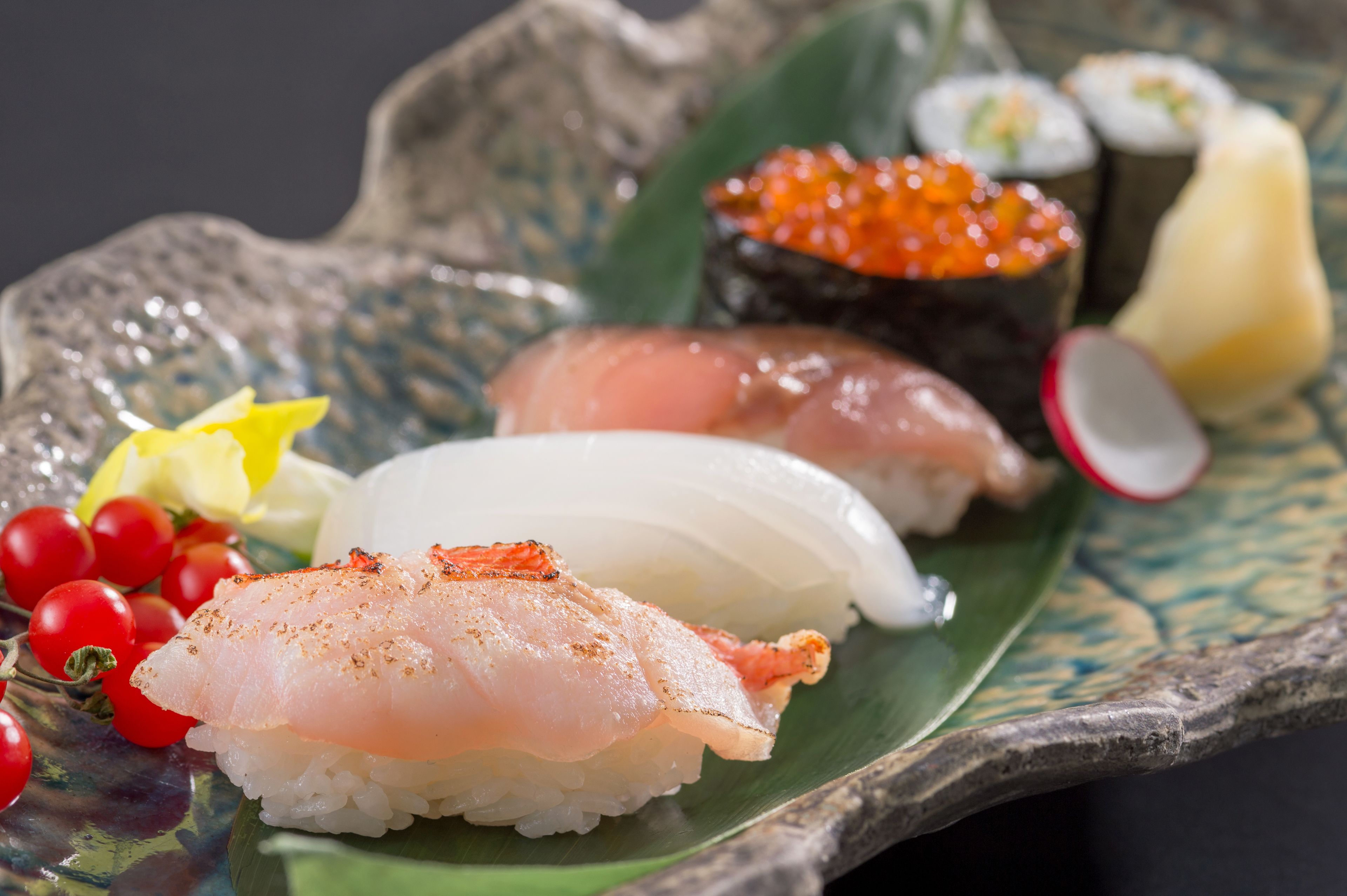 Un plato de sushi con diferentes tipos de pescado y guarniciones, entre ellas salmón, atún y huevas, presentado en un plato decorativo.