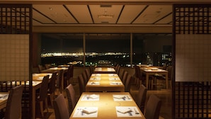 Un restaurant doté de nombreuses tables et chaises, avec de grandes fenêtres offrant une vue sur la ville, en particulier la nuit.