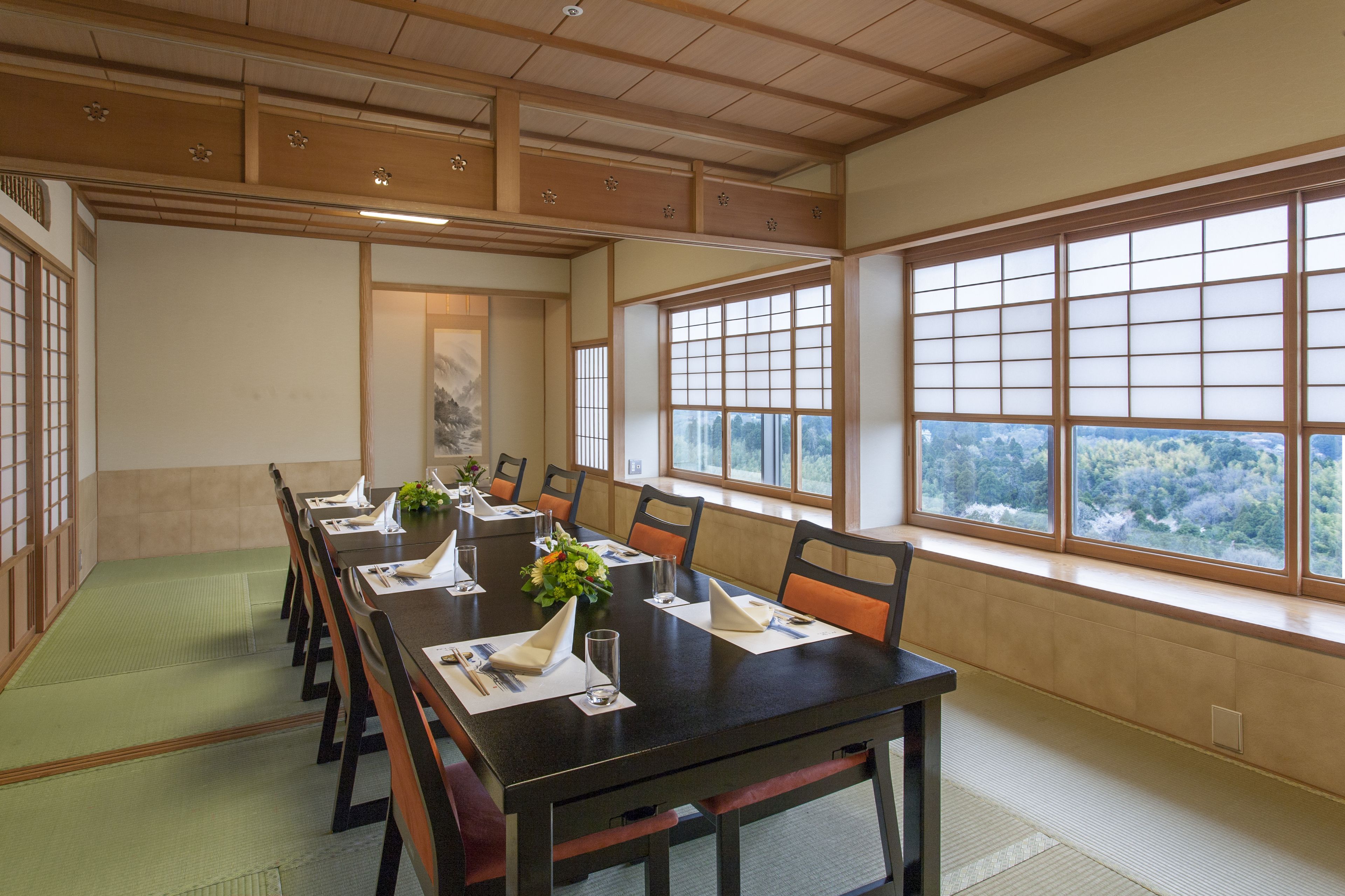 A traditional Japanese-style meeting room with tatami mats, a long table, and large windows offering a view of the forest.