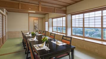A traditional Japanese-style meeting room with tatami mats, a long table, and large windows offering a view of the forest.