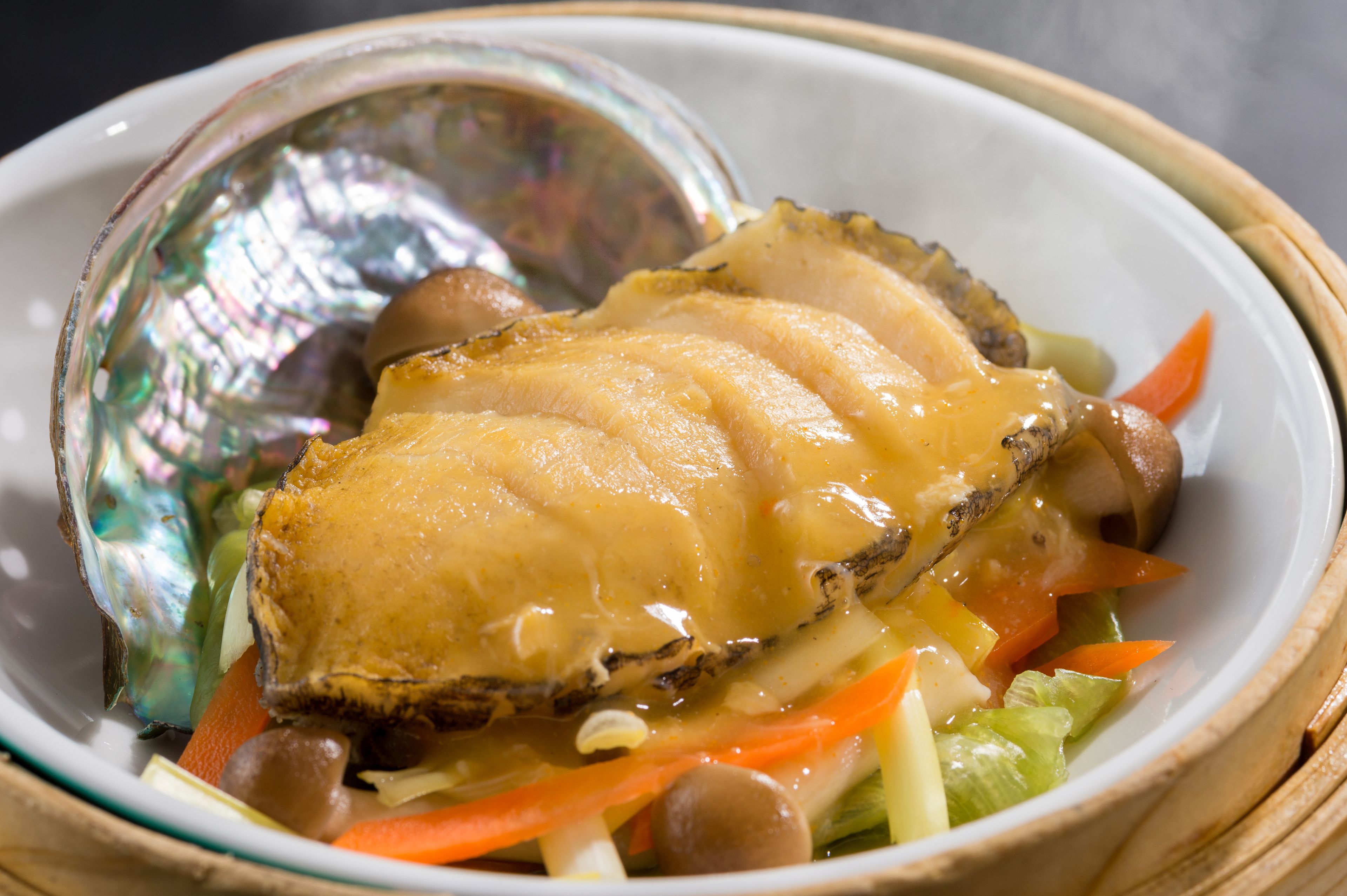 A bowl of food with a clam shell, chicken, and vegetables.