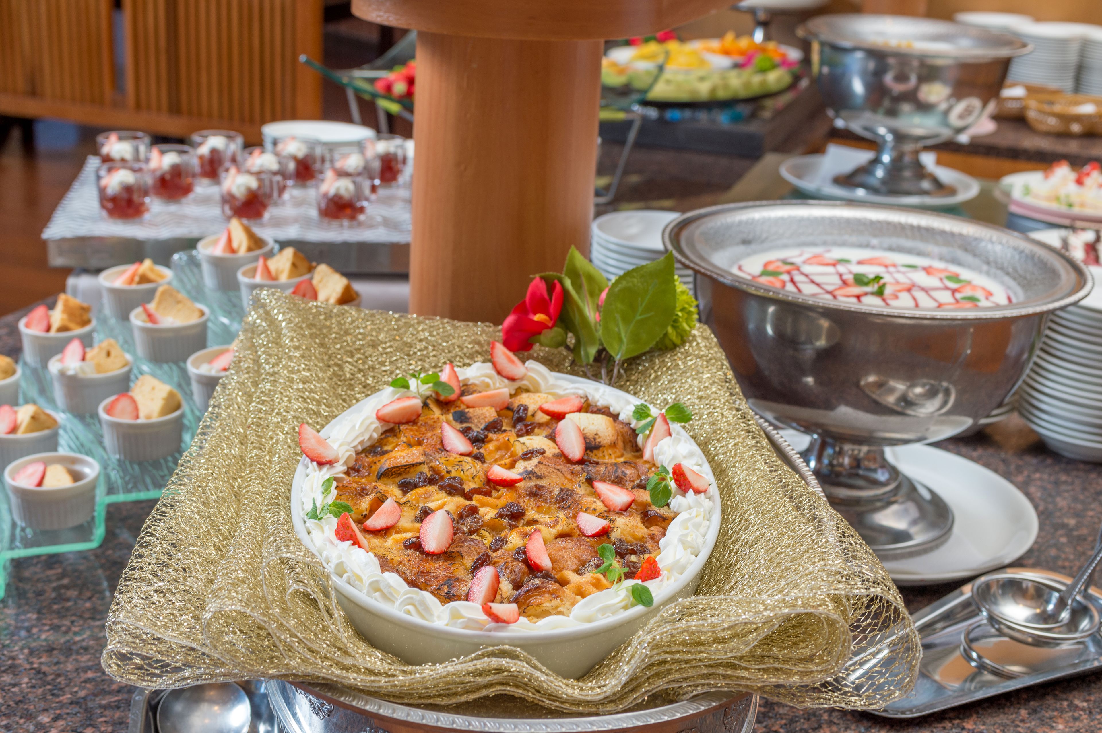 A buffet table with various dishes, including a large bowl of dessert garnished with strawberries and mint leaves, and smaller cups of food.