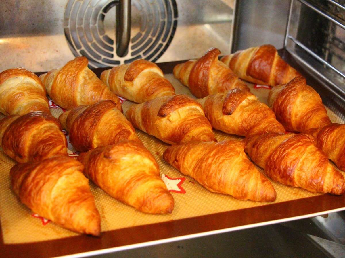 Een dienblad met versgebakken croissants op een bakplaat.