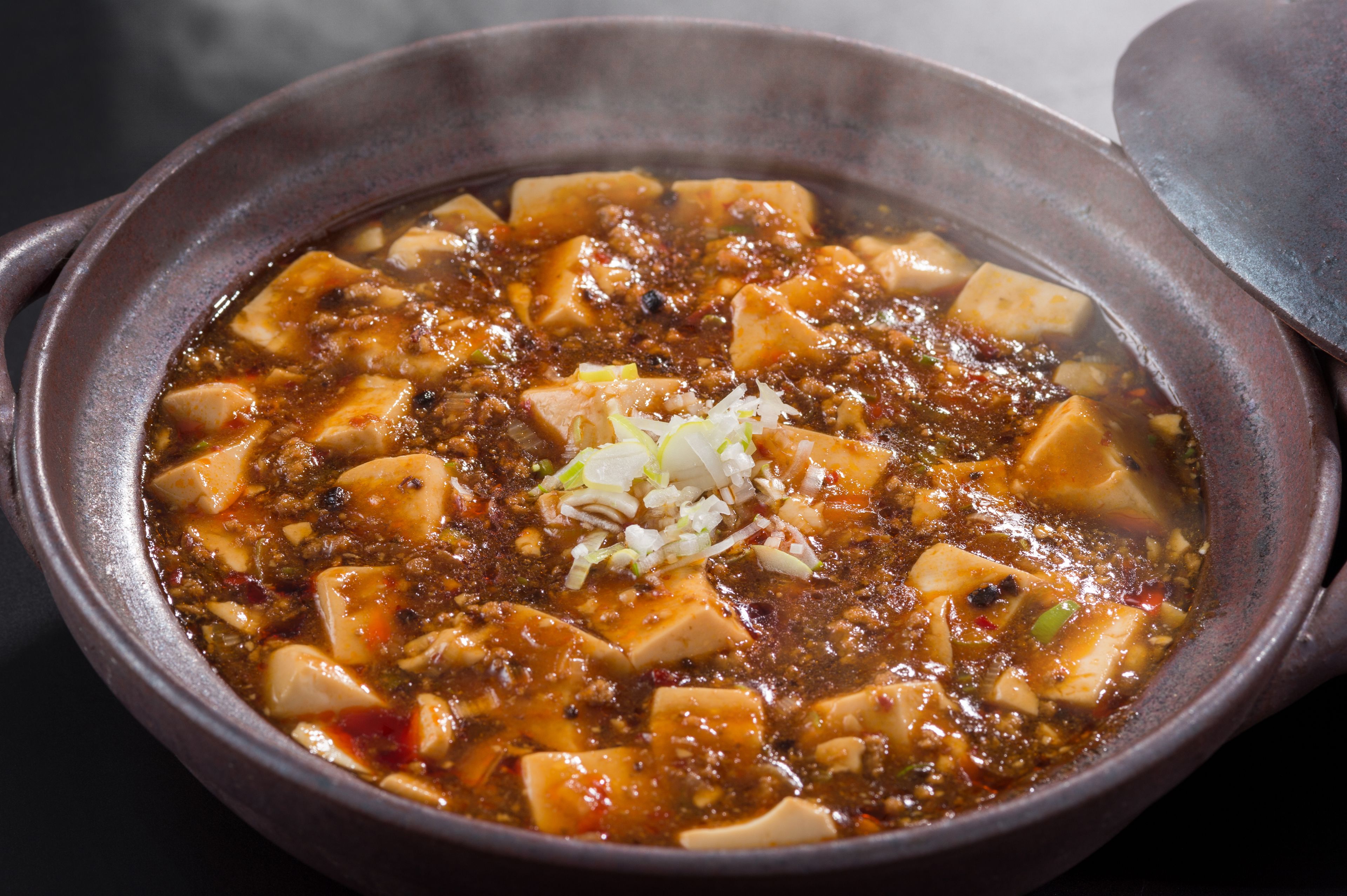A close-up of a hot pot with tofu and vegetables in a rich, spicy broth.