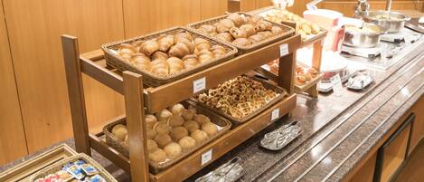 A buffet counter with various food items including bread, waffles, and pastries.