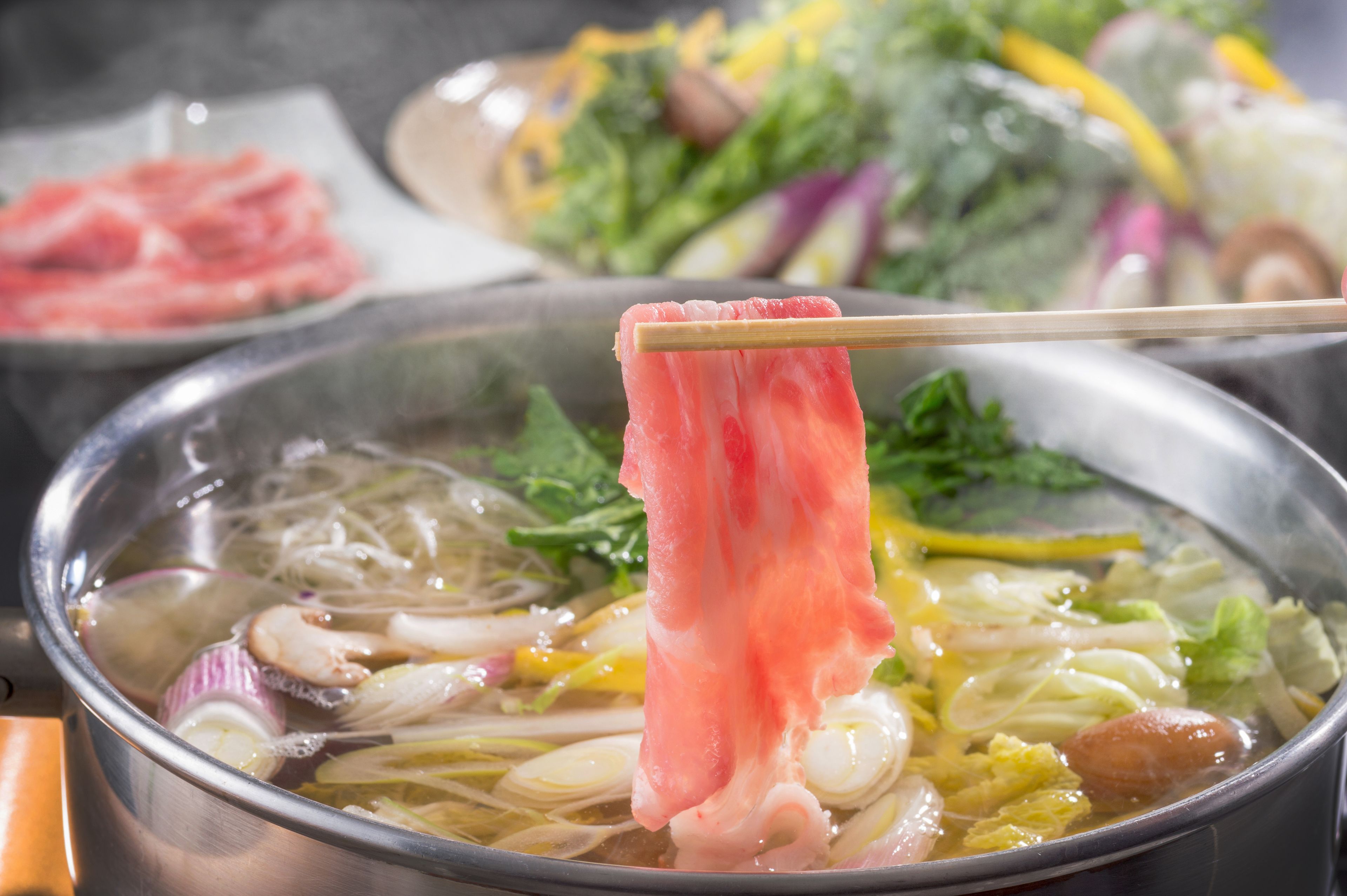A bowl of soup with various vegetables and meat, held by chopsticks.