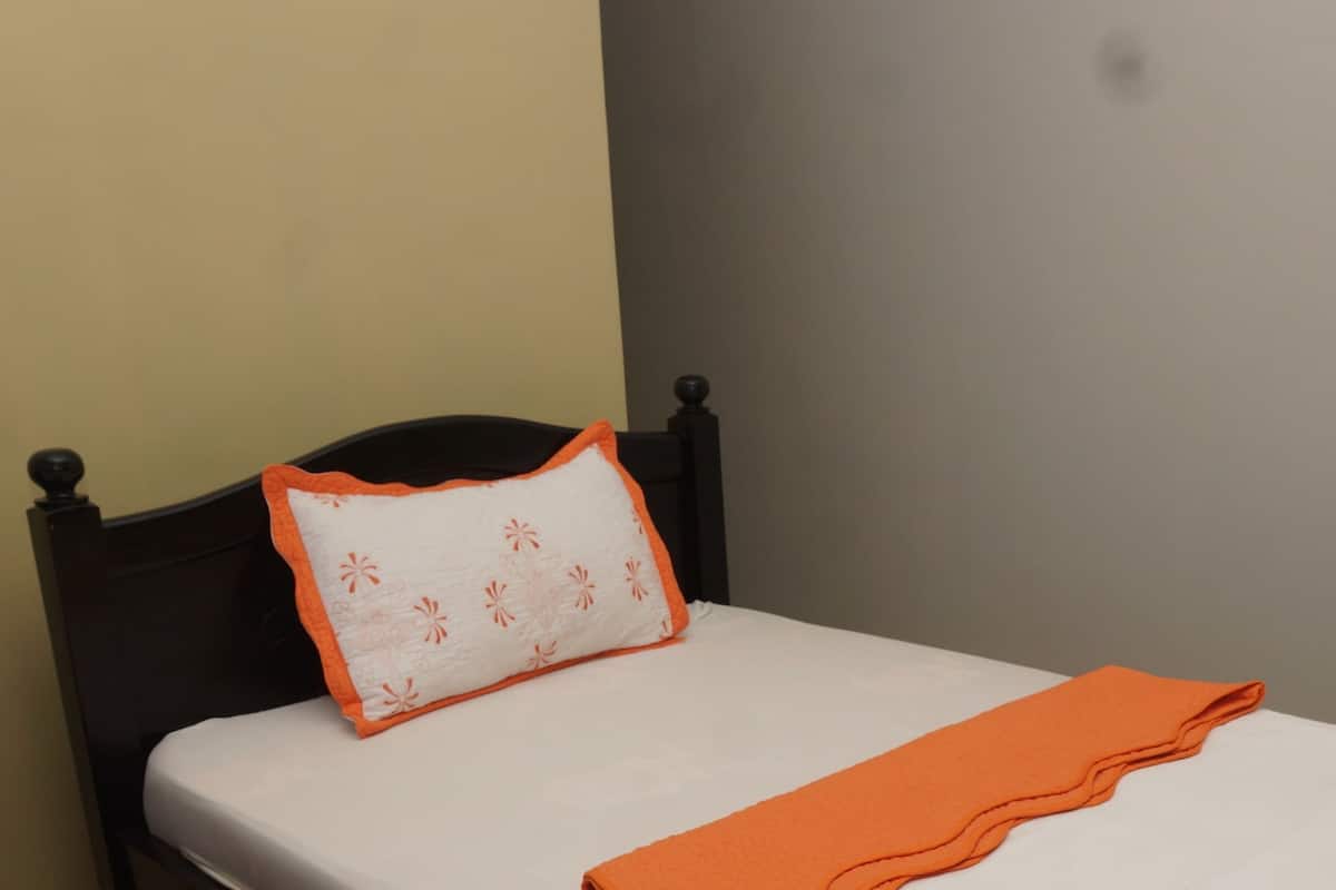 A bed with a white mattress, an orange blanket, and a pillow with a floral pattern.
