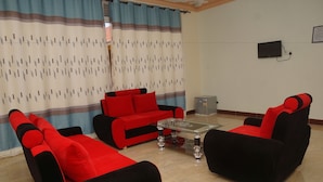 A living room with a red sofa set, a glass coffee table, and a television mounted on the wall. - Oasis Top Hotel (Kampala)