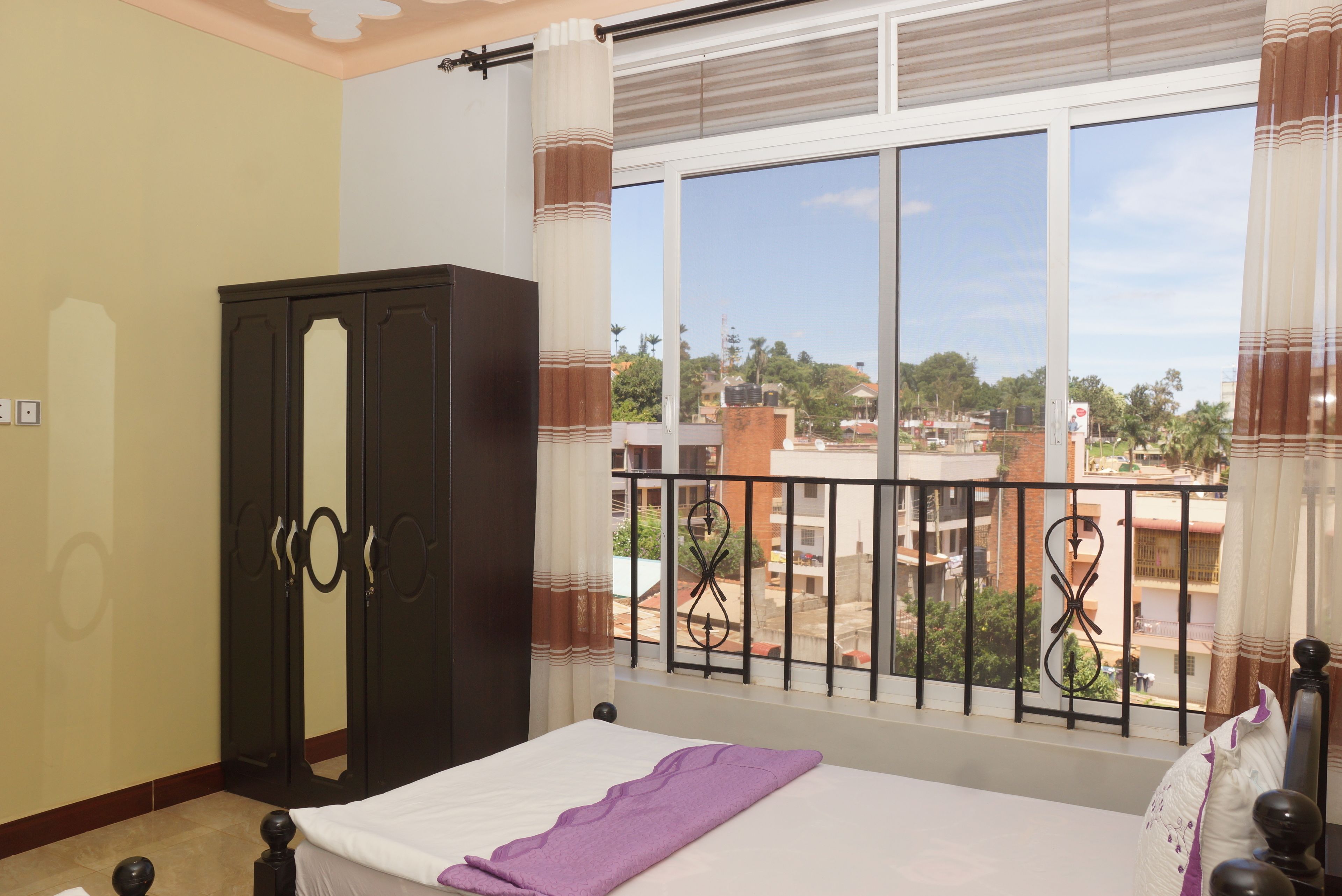A bedroom with a large window, a bed, a wardrobe, and a view of the cityscape.