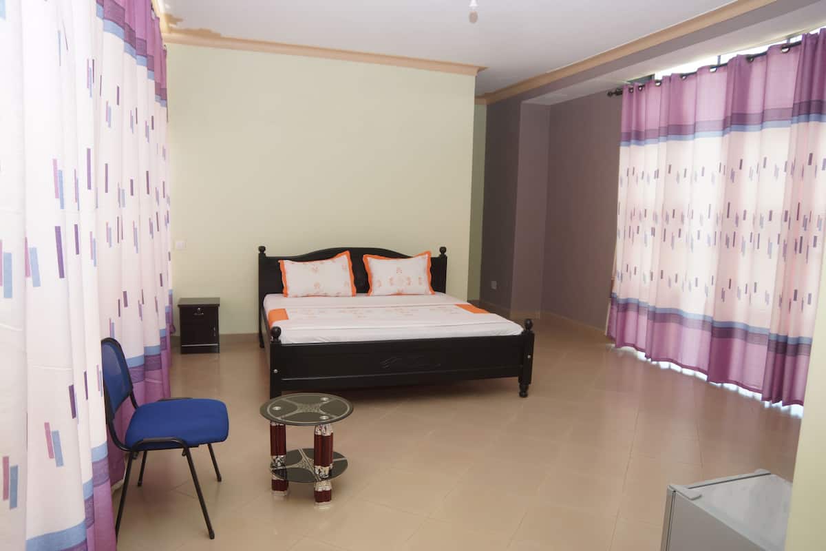 A bedroom with a bed, chair, bedside table, and curtains.