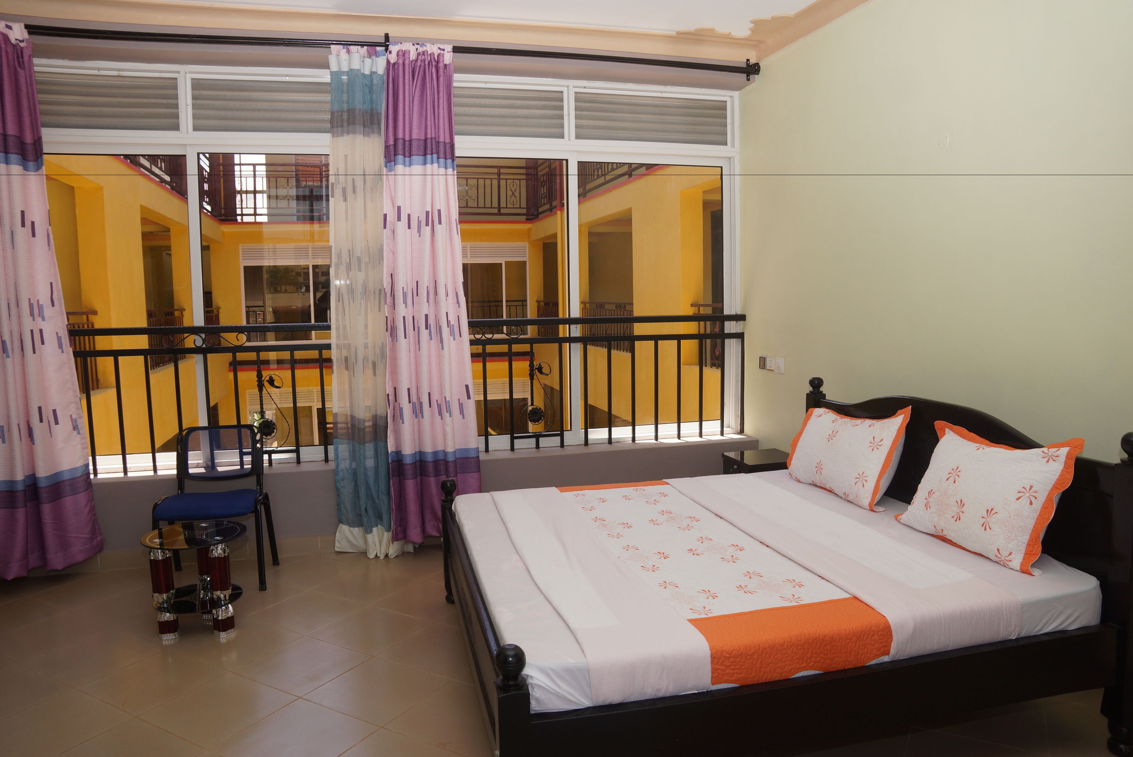 Un dormitorio con cama, una mesita, una silla y un balcón con barandilla.