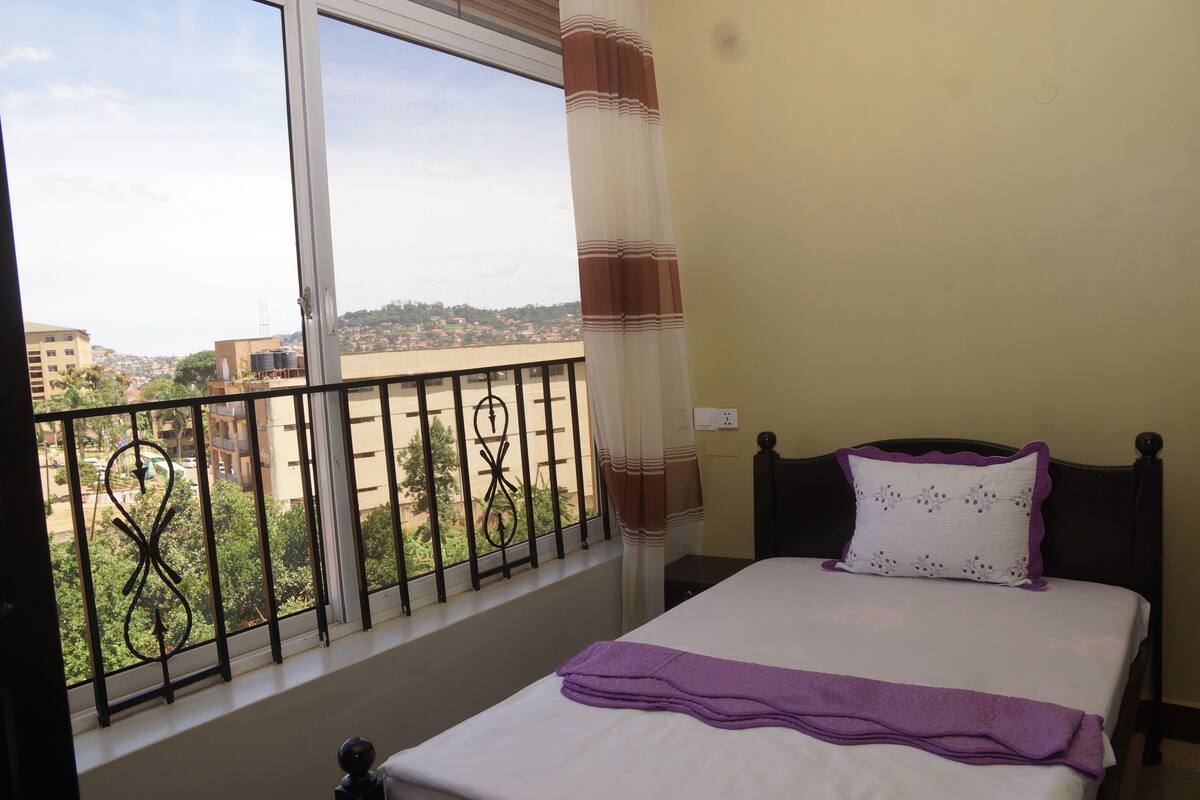 A bedroom with a bed, a window with a view of buildings, and a curtain.
