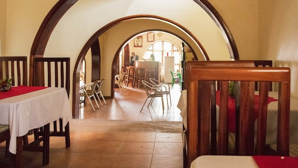 Un interior con un arco alto que da a un comedor con sillas y mesas.
