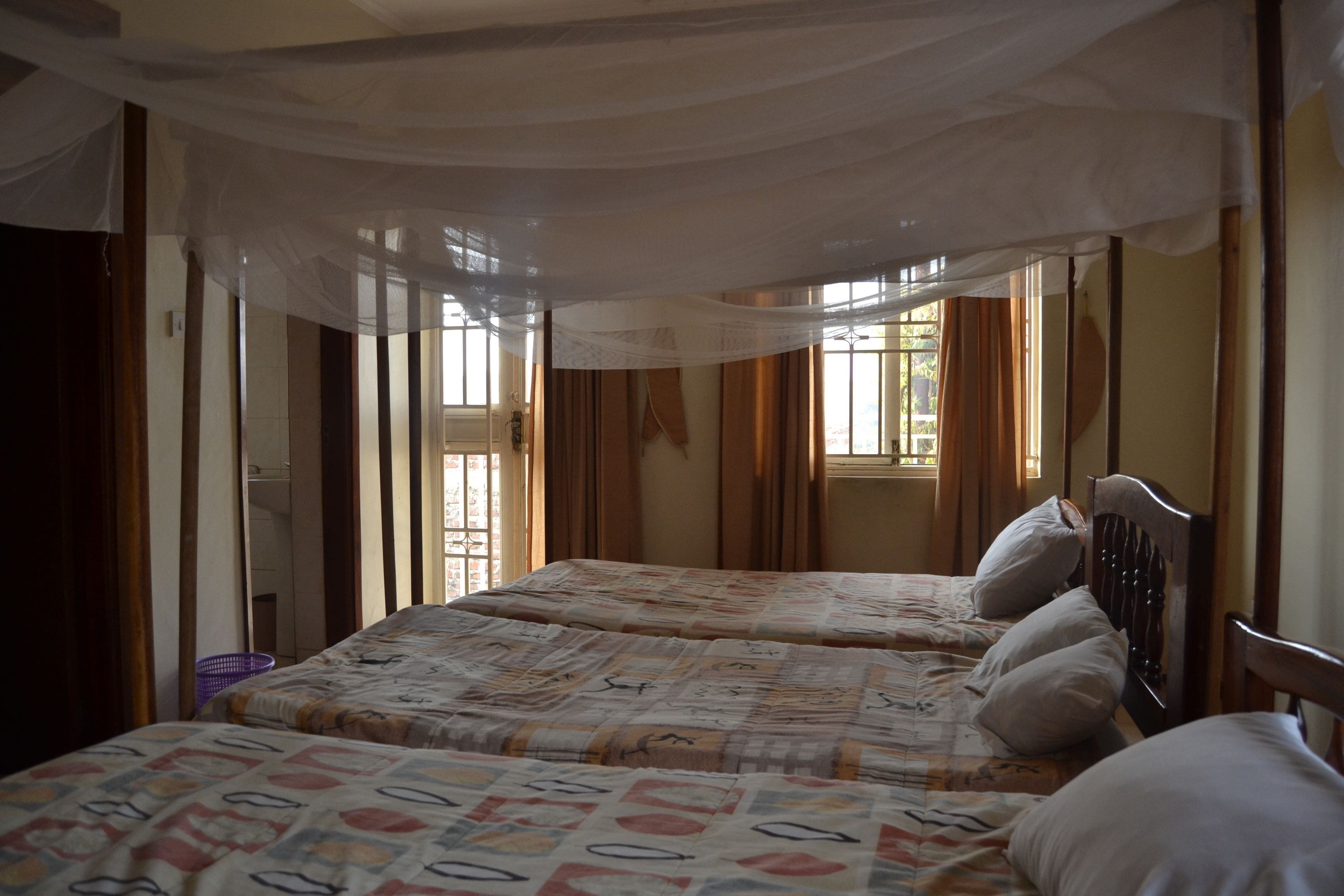 Une chambre avec deux lits, un panier violet et des rideaux transparents.
