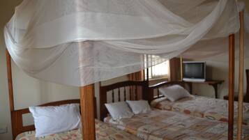 A room with two wooden beds, each with white pillows and patterned bedding. A canopy bed is in the foreground.